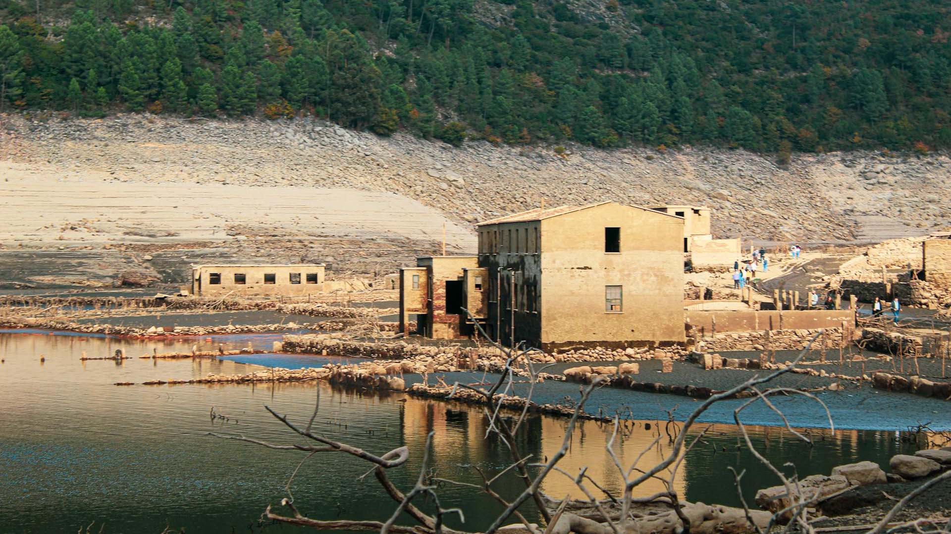 Ruinas del pueblo de Aceredo (provincia de Galicia), con casas abandonadas, agua en primer plano y montañas arboladas al fondo. El pueblo ha emergido tras la sequía del embalse de Lindoso en la frontera entre España y Portugal (península Ibérica).
