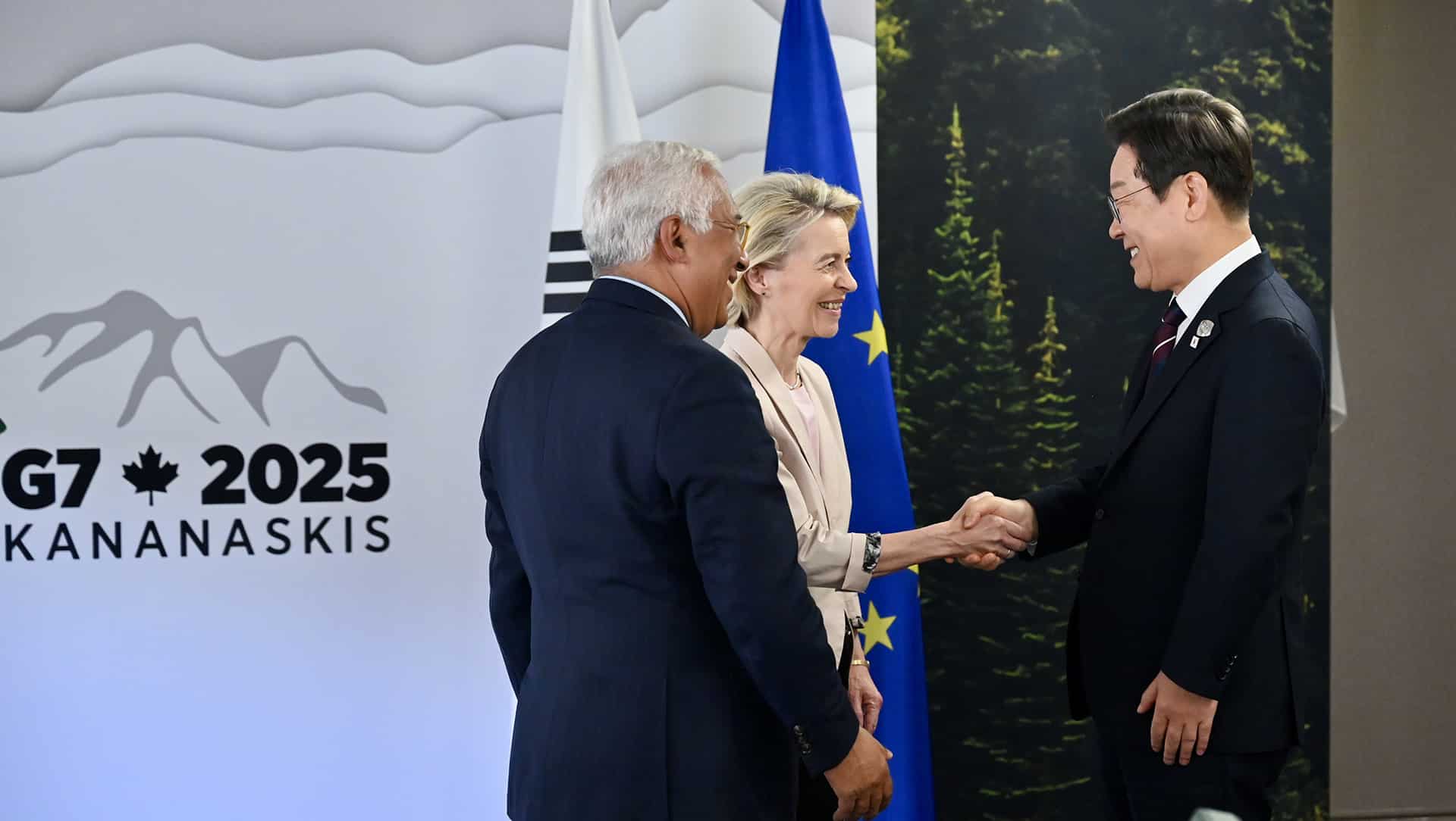 Handshake between Lee-Jae Myung, President of South Korea (on the right), and Ursula Von der Leyen, in the presence of Antonio Costa (on the left). They are standing in front of the flags of South Korea and the European Union, with a background sign reading ‘G7 2025 KANANASKIS’ featuring mountains and a maple leaf.