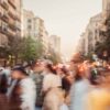 A busy street of Barcelona (Spain) at dusk with blurred motion of people walking. Tall buildings and trees line the street, illuminated by a mix of natural and artificial lighting, creating a lively and bustling atmosphere