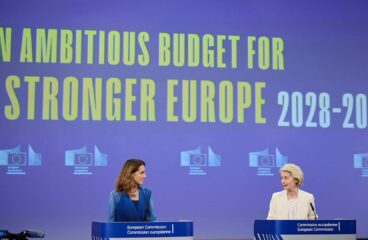 Paula Pinho, portavoz principal de la Comisión Europea (a la izquierda) y Ursula von der Leyen, presidenta de la Comisión Europea (a la derecha) hablando desde los atriles ante la prensa durante el resumen de la reunión semanal de la Comisión sobre el próximo presupuesto de la UE. A la izquierda se asoma una cámara de televisión y al fondo la pantalla azul proyecta el logo de la Comisión en fila y las palabras en inglés “An ambituos budget for a stronger Europe 2028-2034” (un presupuesto ambicioso para una Europa más fuerte 2028-2034).
