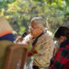 Sushila Karki, exmagistrada y primera ministra interina de Nepal elegida vía Discord, interviene en la Cumbre por la Democracia organizada por la embajada de EEUU en Katmandú en 2021. Está sentada con un micrófono en mano al lado de otras dos mujeres que están fuera de foco. Al fondo, el jardín del lugar del evento.