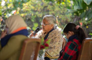 Sushila Karki, exmagistrada y primera ministra interina de Nepal elegida vía Discord, interviene en la Cumbre por la Democracia organizada por la embajada de EEUU en Katmandú en 2021. Está sentada con un micrófono en mano al lado de otras dos mujeres que están fuera de foco. Al fondo, el jardín del lugar del evento.