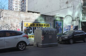 Propaganda electoral y graffitis en una calle de Buenos Aires (Argentina) en 2023. En primer plano, coches aparcados y al centro un container de basura con la leyenda “Si la patria sos vos hacete cargo”. En la pared de detrás, un cartel de Santiago Cúneo, candidato presidencial que promete una Argentina “a lo Bukele”, y a la derecha el cartel de Alejandro Biondini (h), candidato del partido neonazi Bandera Vecinal.
