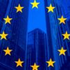 Flag of the European Union against a backdrop of modern glass buildings.