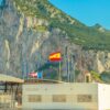 Border between Spain and Gibraltar with the Rock in the background, customs building in the foreground, and several flags flying on top (Spain, the UK, Gibraltar and the EU).