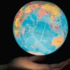 Mano sosteniendo un globo terráqueo iluminado con el océano Índico en el centro, rodeado por África, Asia y Australia, sobre fondo oscuro. Foto: Greg Rosenke (@greg_rosenke).