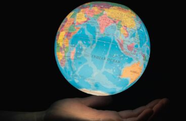 Mano sosteniendo un globo terráqueo iluminado con el océano Índico en el centro, rodeado por África, Asia y Australia, sobre fondo oscuro. Foto: Greg Rosenke (@greg_rosenke).