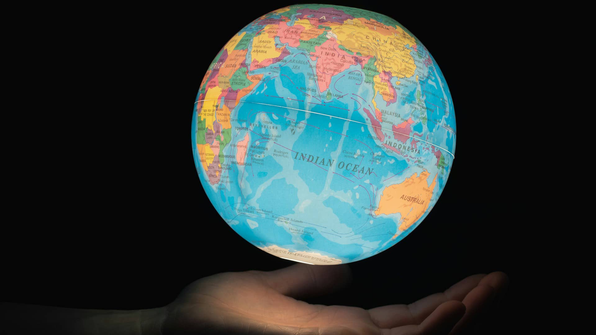 Mano sosteniendo un globo terráqueo iluminado con el océano Índico en el centro, rodeado por África, Asia y Australia, sobre fondo oscuro. Foto: Greg Rosenke (@greg_rosenke).