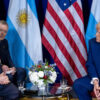 Javier Milei, su traductor, y Donald Trump durante el encuentro entre ambos mandatarios en el Gaylord National Resort & Convention Center de Oxon Hill, Maryland (22/02/2025). Al fondo, las banderas de Argentina y Estados Unido y un arreglo floral sobre la mesa en el centro.