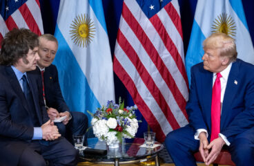 Javier Milei, su traductor, y Donald Trump durante el encuentro entre ambos mandatarios en el Gaylord National Resort & Convention Center de Oxon Hill, Maryland (22/02/2025). Al fondo, las banderas de Argentina y Estados Unido y un arreglo floral sobre la mesa en el centro.