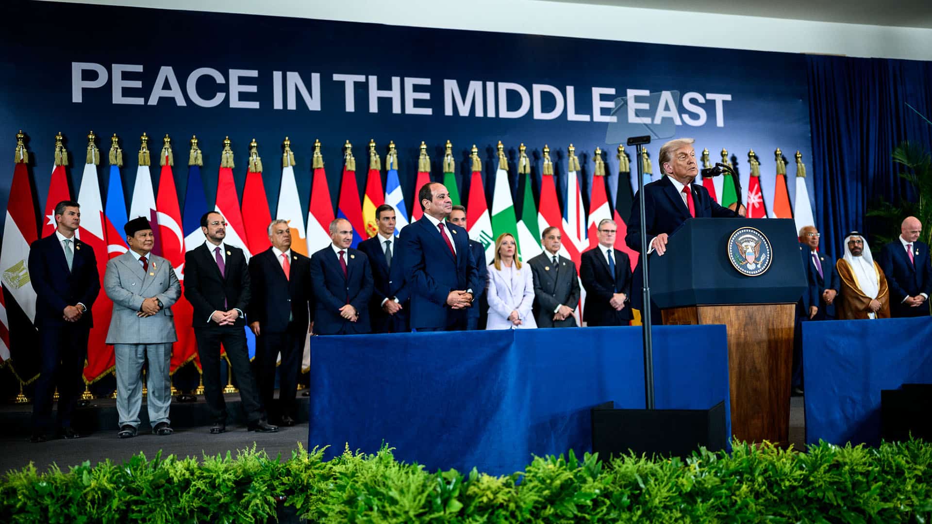 Donald Trump pronuncia su discurso desde el atril tras la firma del acuerdo de alto el fuego entre Israel y Hamás para el fin a la guerra en Gaza durante la cumbre en Sharm el Sheij, Egipto (13/10/2025). Detrás, los líderes mundiales que han acudido al encuentro, de pie, y al fondo banderas de los países representados con una pantalla con las palabras “Peace in the Middle East”.