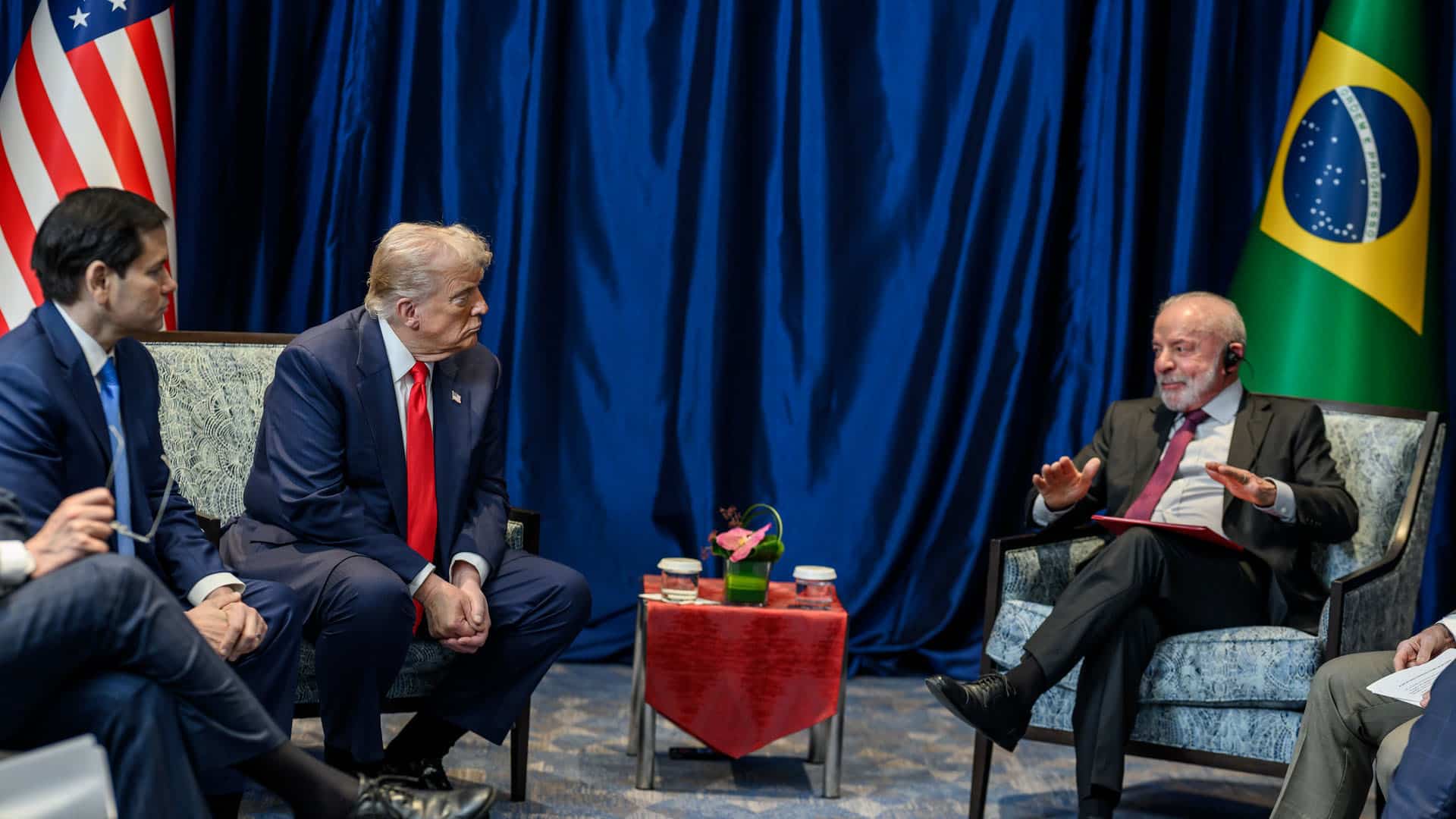Reunión entre delegaciones de Estados Unidos y Brasil durante la Cumbre de la ASEAN en Kuala Lumpur, Malasia (25/10/2025). De izquierda a derecha: marco Rubio, Donald Trump y Luiz Inácio da Silva. Entre Trump y Da Silva, una mesa pequeña con mantel rojo y flores. Al fondo, banderas de ambos países.