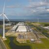Vista aérea de parque eólico y un centro de datos junto a un cuerpo de agua, con turbinas y edificios en el puerto marítimo de Eemshaven, al norte de Países Bajos.
