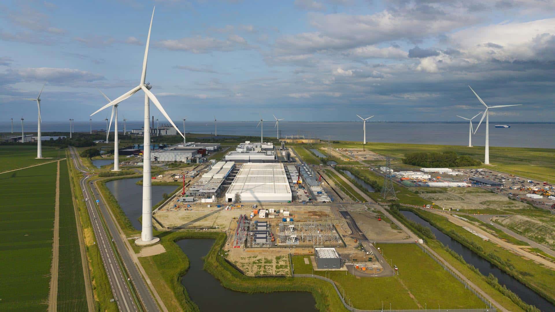Vista aérea de parque eólico y un centro de datos junto a un cuerpo de agua, con turbinas y edificios en el puerto marítimo de Eemshaven, al norte de Países Bajos.