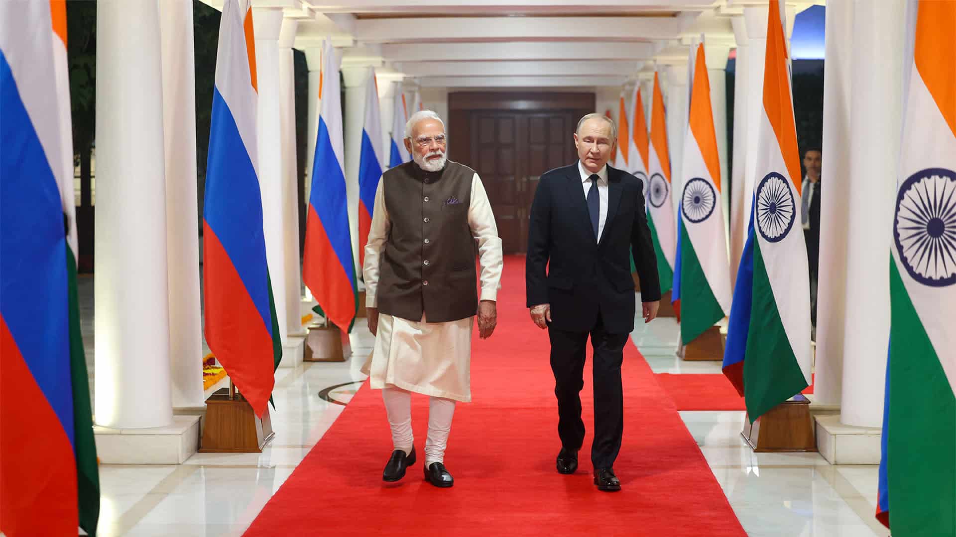 A la izquierda, Narendra Modi, primer ministro de India, y, a la derecha, Vladímir Putin, presidente de la Federación de Rusia, el 4 de diciembre en la residencia oficial del primer ministro en Nueva Delhi (7 Lok Kalyan Marg). Ambos caminan sobre una alfombra roja, flanqueada por banderas rusas en el lado de Modi y banderas indias en el lado de Putin.