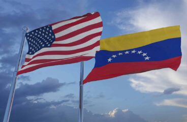 Las banderas de Estados Unidos y Venezuela ondeando en un cielo claro. En primer plano, la bandera de Estados Unidos, y, en segundo plano, la de Venezuela, ondean sobre los mástiles con un cielo claro, con algunas nubes.