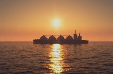 Buque cisterna de GNL al atardecer en el mar en Rusia (28/04/2020). Un cielo anaranjado muy vibrante ilumina la escena, que se refleja en el mar, en contraposición al buque cisterna, que aparece como una sombra sobre el agua.