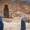 Dos mujeres caminan cubiertas con burkas de color azul en Bamiyán, provincia de Afganistán en 2012. Al fondo del paisaje árido, una cadena de montañas con una cavidad vacía donde se erguía uno de los Budas de Bamiyán construidos en los años 507 y 554 d.C. y destruidos por los talibanes en 2001.
