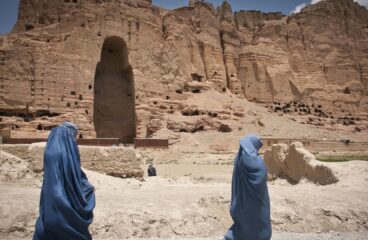 Dos mujeres caminan cubiertas con burkas de color azul en Bamiyán, provincia de Afganistán en 2012. Al fondo del paisaje árido, una cadena de montañas con una cavidad vacía donde se erguía uno de los Budas de Bamiyán construidos en los años 507 y 554 d.C. y destruidos por los talibanes en 2001.