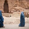 Dos mujeres caminan cubiertas con burkas de color azul en Bamiyán, provincia de Afganistán en 2012. Al fondo del paisaje árido, una cadena de montañas con una cavidad vacía donde se erguía uno de los Budas de Bamiyán construidos en los años 507 y 554 d.C. y destruidos por los talibanes en 2001.