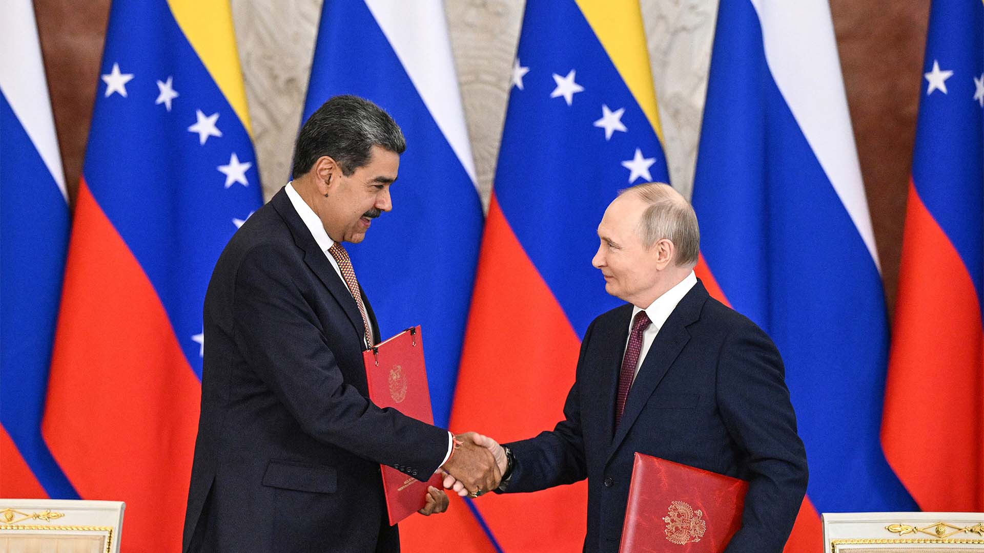 A la izquierda, Nicolás Maduro, expresidente de Venezuela, da la mano a Vladimir Putin, presidente de Rusia, en el Palacio del Kremlin, en Moscú (07/05/2025). Ambos portan una carpeta roja con el tratado de cooperación que acaban de firmar. Al fondo, varias banderas de Rusia y Venezuela.