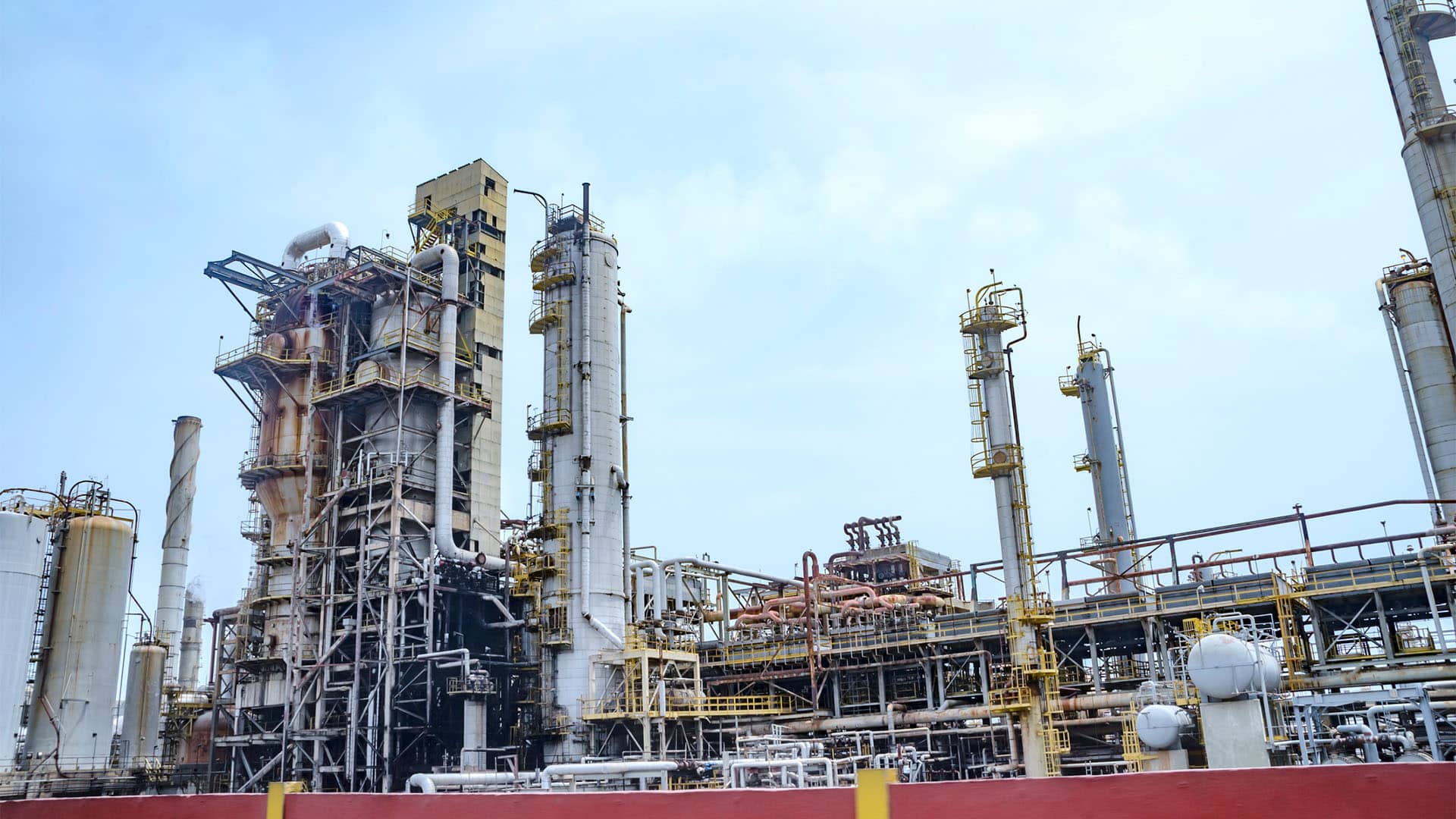 Planta de refinería de petróleo El Palito en Puerto Cabello (Estado Carabobo, Venezuela). En la imagen, múltiples torres de destilación de petróleo, hornos y una gran cantidad de sistemas de tuberías interconectados para su procesamiento. Al fondo, el cielo claro con algunas nubes.