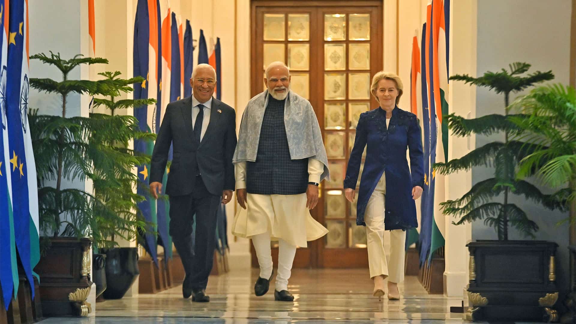 De izquierda a derecha: António Costa, presidente del Consejo Europeo; Narendra Modi, primer ministro de la India; y Ursula von der Leyen, presidenta de la Comisión Europea, caminan en la Casa Hyderabad, Nueva Dehli (27/01/2026). A ambos lados, múltiples banderas de la Unión Europea y la India y varias plantas.