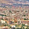 Vista aérea de la ciudad de Murcia. Cientos de edificios de diferentes alturas y colores, donde destaca la torre de la Catedral de la ciudad, en el centro, de color amarronado. Al fondo, algunas concentraciones de árboles y vegetación, aunque el paisaje es árido.