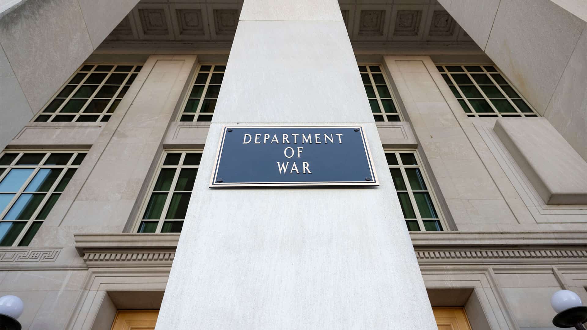 Placa negra con letras doradas con el texto “Departamento de Guerra” en el edificio del Pentágono (13/11/2025) durante su instalación, por parte del secretario Pete Hegseth. Tras la placa, puede verse parte de la entrada del edificio principal, de piedra de color blanco y dos puertas de madera.