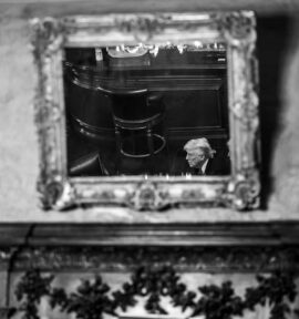 Foto en blanco y negro del reflejo del presidente Donald Trump en un espejo enmarcado de una sala de conferencias con una decoración barroca en el Club Mar-a-Lago de Palm Beach, Florida.