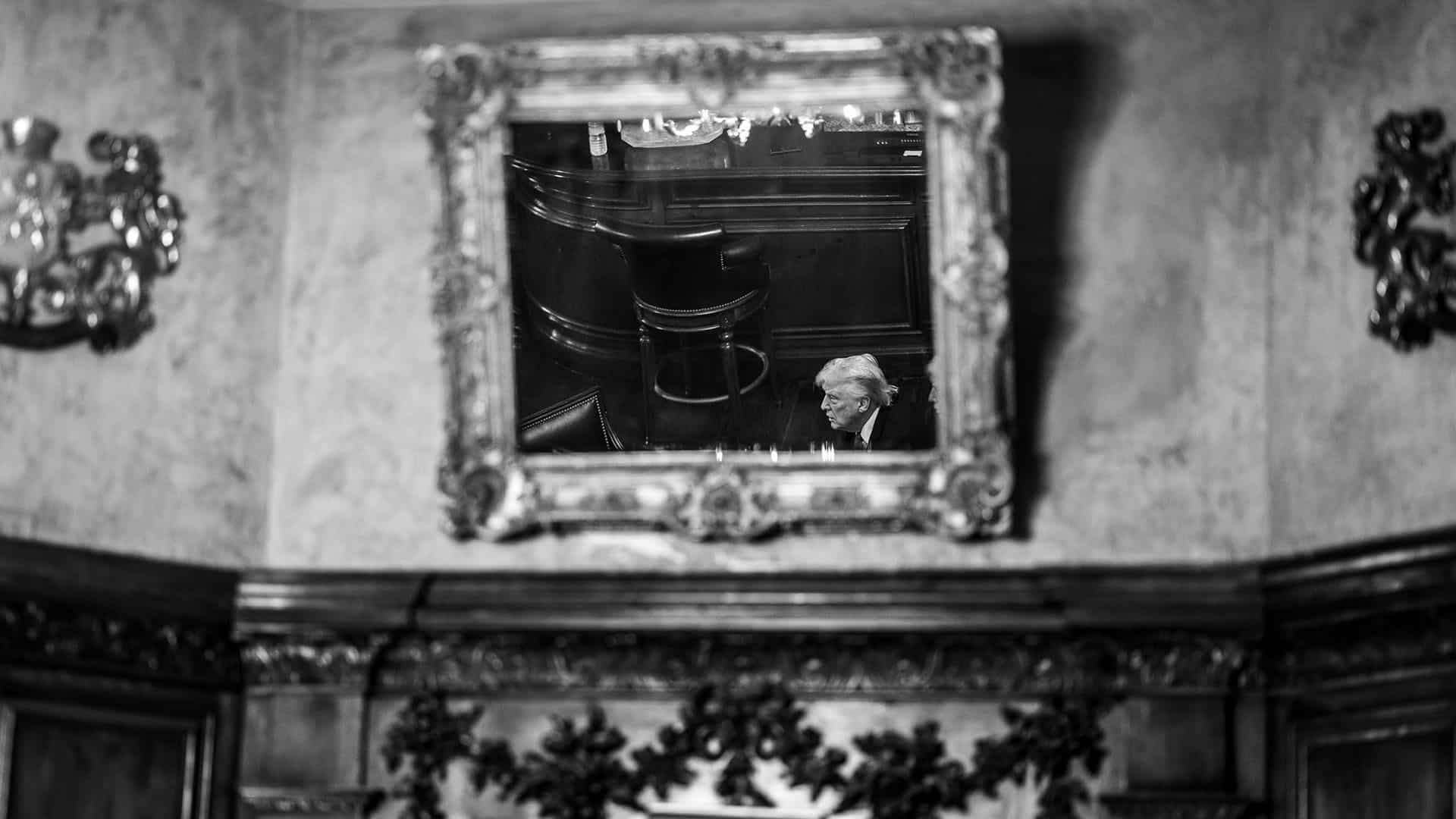 Foto en blanco y negro del reflejo del presidente Donald Trump en un espejo enmarcado de una sala de conferencias con una decoración barroca en el Club Mar-a-Lago de Palm Beach, Florida.