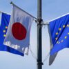 Mástil con las banderas de la Unión Europea y Japón, durante la visita de Kaja Jallas a Japón en julio de 2025. El mástil tiene cuatro postes con cuatro banderas, dos de la UE y dos de Japón. Detrás de las banderas, un edificio blanco con numerosas ventanas y un cielo completamente azul y despejado.