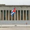 Vista de la fachada principal del Palacio de la Revolución, sede de la presidencia y gobierno de la República de Cuba. La fachada cuenta con múltiples columnas tras la escalinata principal de entrada. En el centro de la imagen, la bandera de Cuba ondea en un mástil.