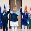 From left to right: António Costa, President of the European Council; Narendra Modi, Prime Minister of India; and Ursula von der Leyen, President of the European Commission, at Hyderabad House, New Delhi, India (27/01/2026). In a gesture of victory, the three representatives raise their hands. On either side, flags of the European Union on the left and India on the right.