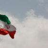 Iranian flag flying in a cloudy sky.