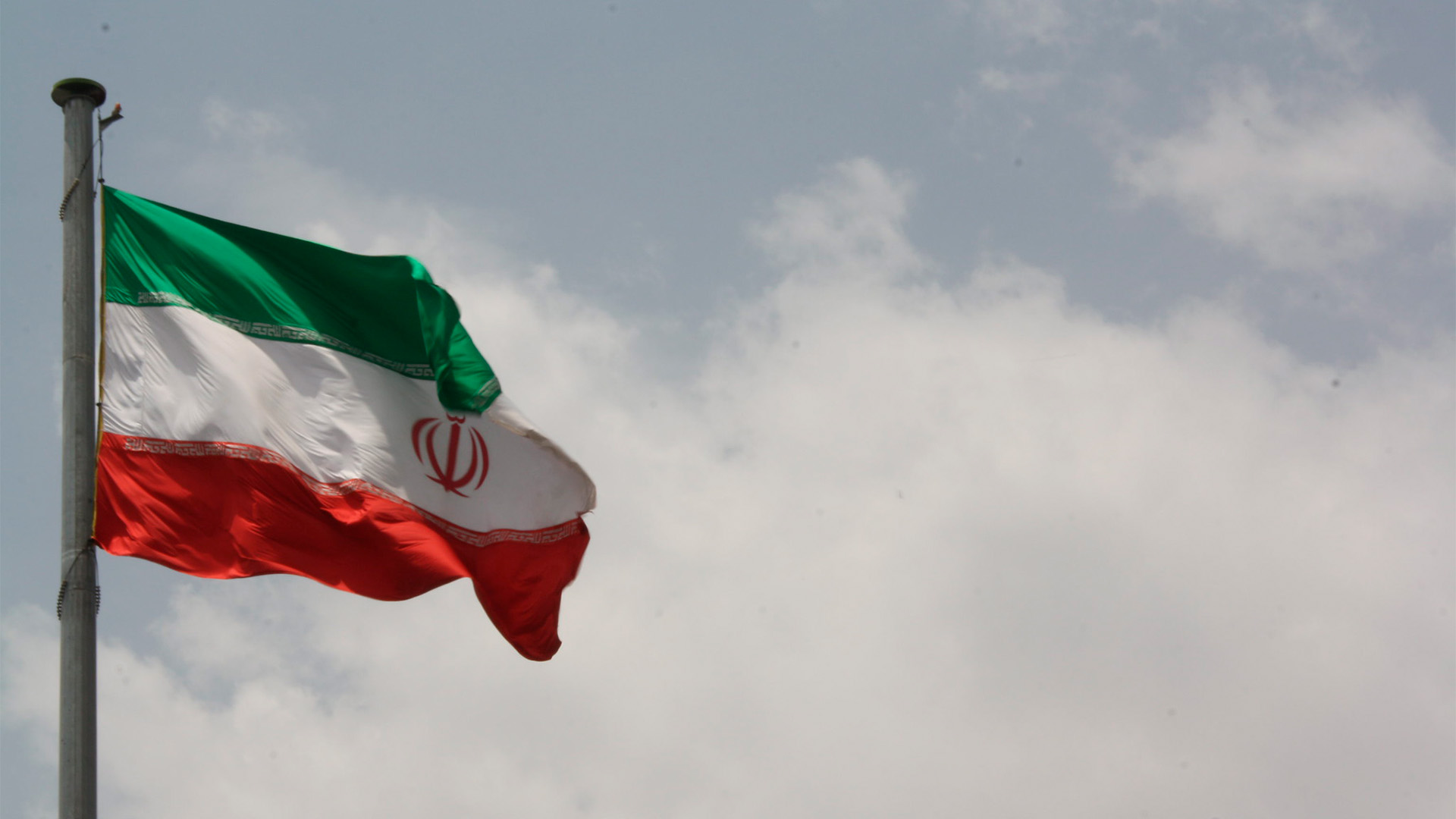 Iranian flag flying in a cloudy sky.