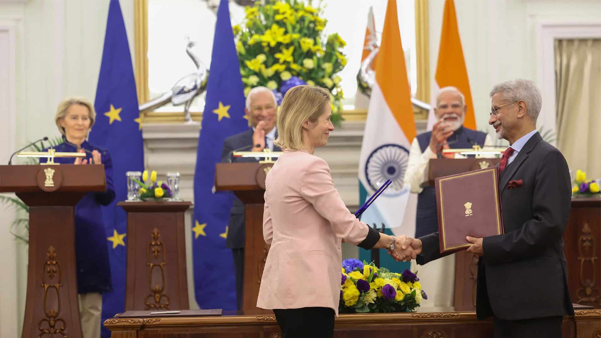 Signing of the India–EU Free Trade Agreement (27/01/2026). Kaja Kallas, EU High Representative for Foreign Affairs and Security Policy, and Dr. Subrahmanyam Jaishankar, Minister of External Affairs of India, sign the bilateral agreement. Behind them, three lecterns where Ursula von der Leyen, President of the European Commission; António Costa, President of the European Council; and Narendra Modi, Prime Minister of India, applaud. In the background, flags of the EU and India and two silver peacocks, the symbol of India, in Hyderabad House, New Delhi.