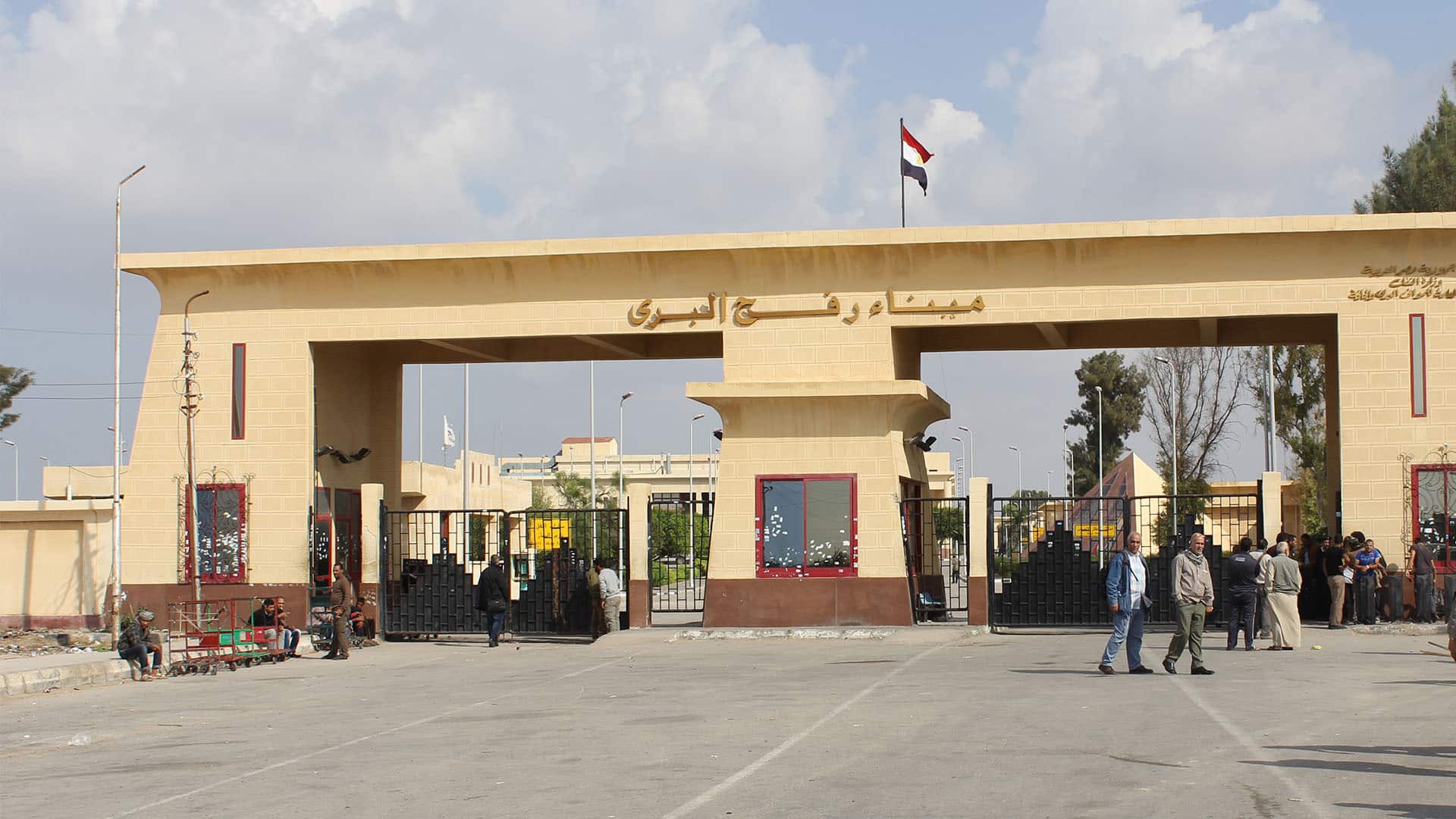 Paso de Rafah, entre la Franja de Gaza y Egipto. El paso es una construcción de ladrillo de color amarillo, con rejas de paso a ambos lados y varias cabinas con ventanas de marco rojo. En la parte superior del paso, la inscripción en árabe “Puerto hebreo de Rafah”, y, en lo alto, la bandera de Egipto.