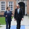 Emmanuel Macron, presidente de Francia, y Friedrich Merz, canciller de Alemania, hablan en la llegada a la reunión informal de los miembros del Consejo Europeo en el castillo de Alden Biesen, en Bélgica. En primer plano, ambos representantes, que caminan por el paseo de acceso, rodeado del verde del césped, y, al fondo, una de las fachadas del castillo, que mezcla el color teja con el gris de las piedras, con una entrada en arco, y varias ventanas.