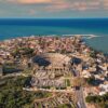 Vista aérea del casco antiguo de Antalya, Turquía, próxima sede de la COP 31. Destaca, en el centro de la imagen, el teatro romano de Aspendos, rodeado de algunas de las ruinas romanas aún conservadas en la ciudad. Detrás, edificios residenciales y, al fondo, parte del puerto y el mar abierto de un color azul intenso. El cielo es claro, aunque algo nublado.