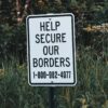 Sign reading “Help Secure Our Borders” with a toll-free number for U.S. Customs and Border Protection, standing on green grass at the Pigeon River boat launch south of the Canadian border.