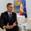 Pedro Sánchez habla en la grabación del vídeo por los 40 años de España en la Unión Europea en una de las salas del Palacio de la Moncloa. El presidente enfatiza con sus manos, sentado en una butaca de color blanco. A su lado, una mesa transparente con un vaso de agua. Al fondo, otro conjunto de butacas y mesa blancas, y, en la pared, varias obras pictóricas y, muy cerca, las banderas de España y la Unión Europea, desenfocadas.