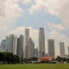 Panorámica del skyline de los rascacielos de Singapur bajo un cielo claro y algo nublado, vistos desde una explanada de césped con algunos árboles.