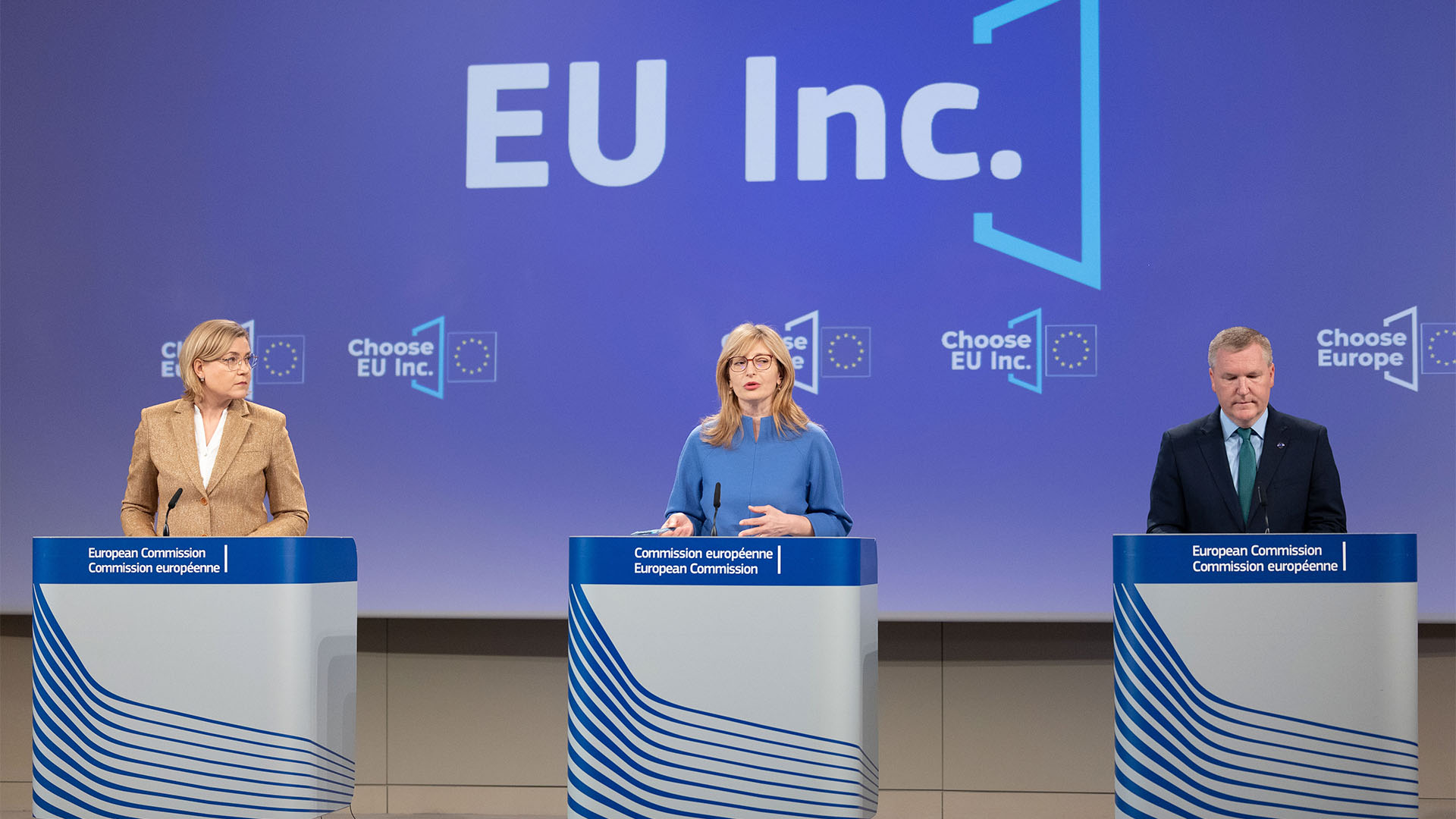 Henna Virkkunen, vicepresidenta ejecutiva de la Comisión Europea; Ekaterina Zaharieva, comisaria de Startups, Investigación e Innovación; y Michael McGrath, comisario de Democracia, Justicia, Estado de Derecho y Protección del Consumidor, comparecen en Bruselas tras la reunión semanal de la Comisión Europea. Intervienen desde un atril con el logotipo de la Comisión (“Commission européenne. European Commission”), mientras en la pantalla de fondo se repite el emblema de EU Inc. sobre el azul institucional de la UE.