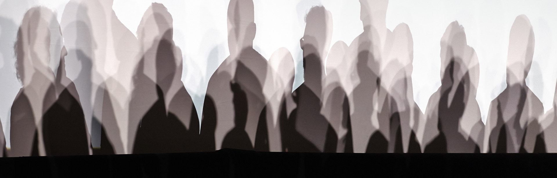 Sombras de una multitud de personas proyectadas en una pared blanca durante un congreso.