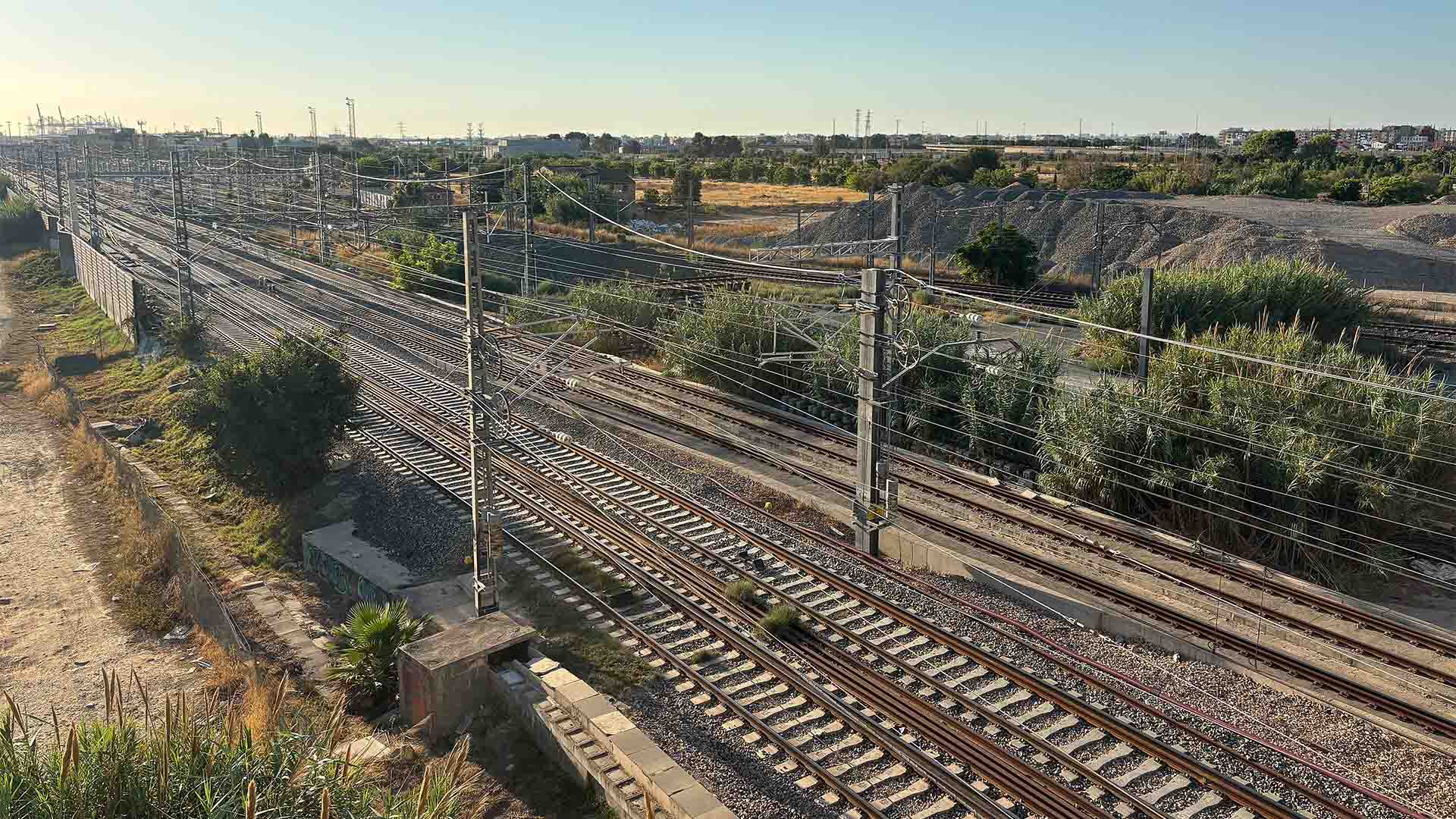 Varias vías ferroviarias electrificadas del Corredor Mediterráneo atraviesan la zona de Malilla, junto a Turia Nova en Valencia, con postes, cables aéreos y vegetación en un entorno periurbano.