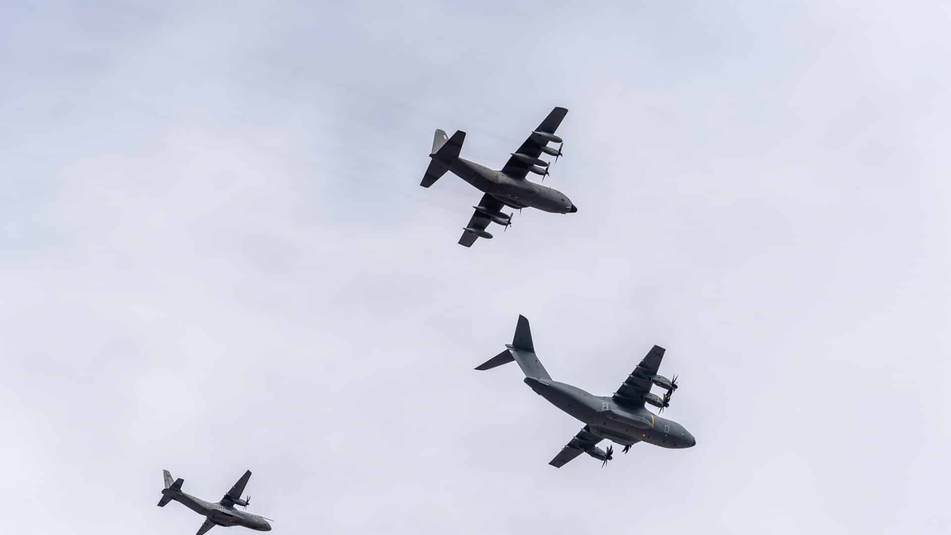 Airbus A-400M, C-130 Hércules y C-295 volando en formación durante el desfile del Ejército en el Día Nacional de España, vistos desde abajo sobre un cielo gris.
