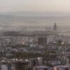 Panoramic view of the city of Sulaymaniyah, in Iraqi Kurdistan, with dense buildings in the foreground and mountains in the background under soft light.