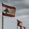 Varias banderas del Líbano ondean en postes a lo largo de la costa en El Mina, Trípoli, bajo un cielo nublado.