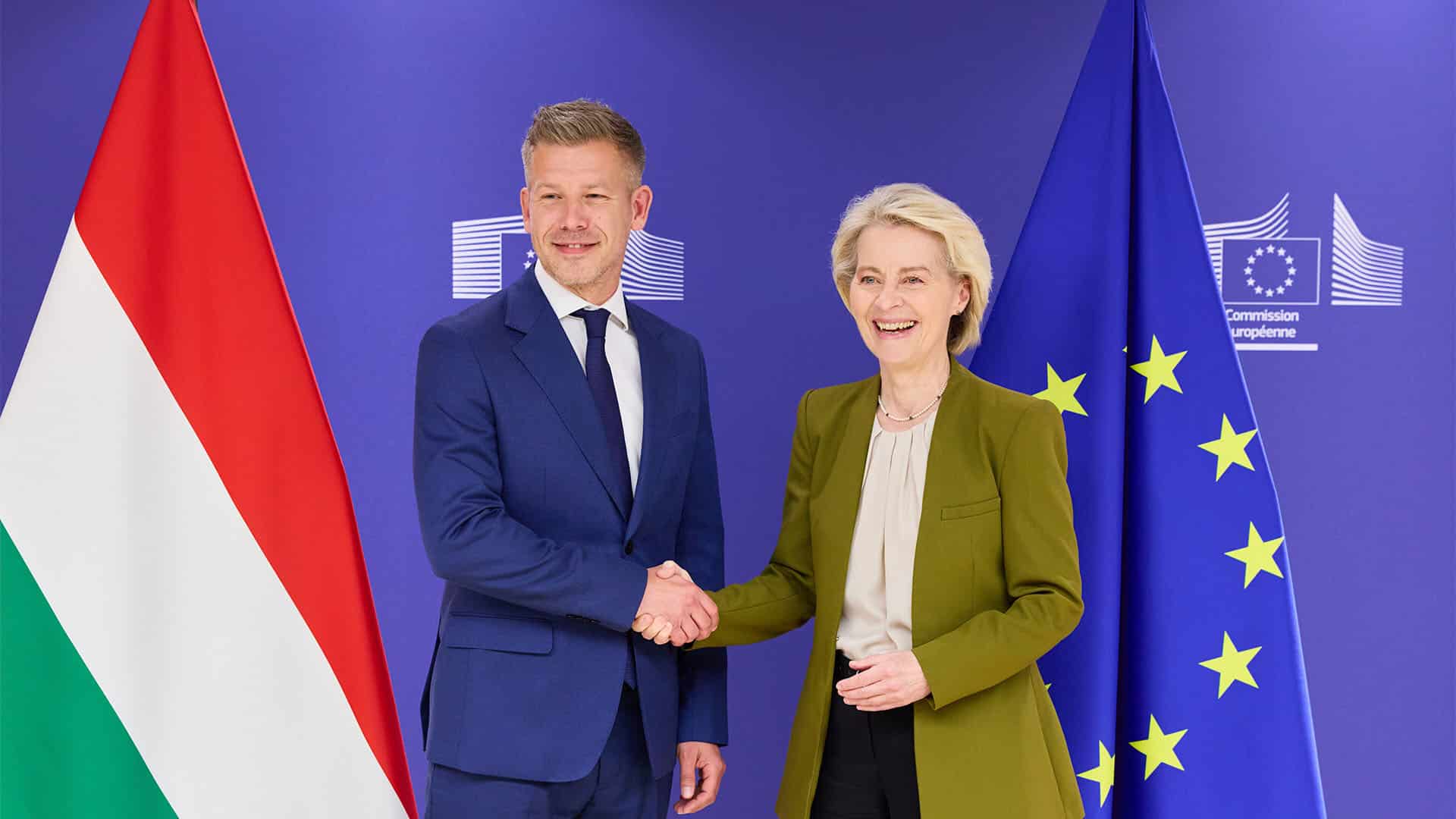 La presidenta de la Comisión Europea, Ursula von der Leyen, estrecha la mano del primer ministro de Hungría, Péter Magyar, durante un encuentro oficial en Bruselas. Ambos posan sonrientes frente a las banderas de la Unión Europea y de Hungría.